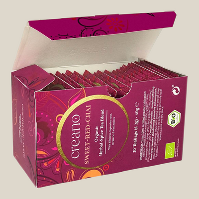 TuanaShop BV Sweet Red Chai biologische kruidenthee in een open doosje met 20 theezakjes en hibiscus en specerijen.